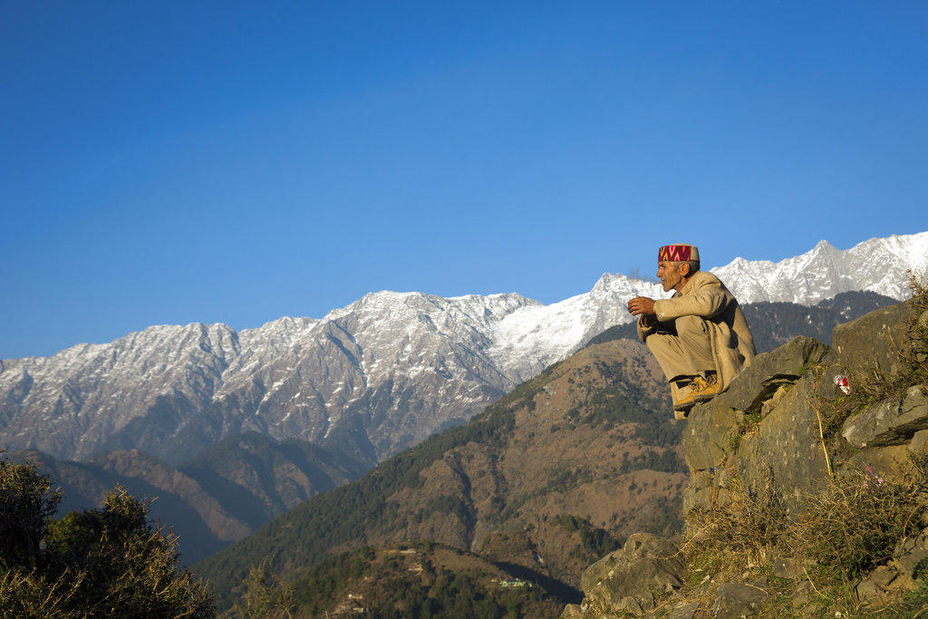 A man rests for a smoke against the backdrop of the Dhauladhar range of the Himalayas in Dharmsala - AP