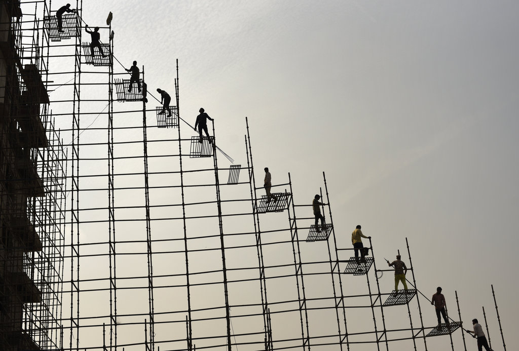 Indian laborers stand on scaffolding shift steel rods from the ground to the top of an under construction hospital building  - AP