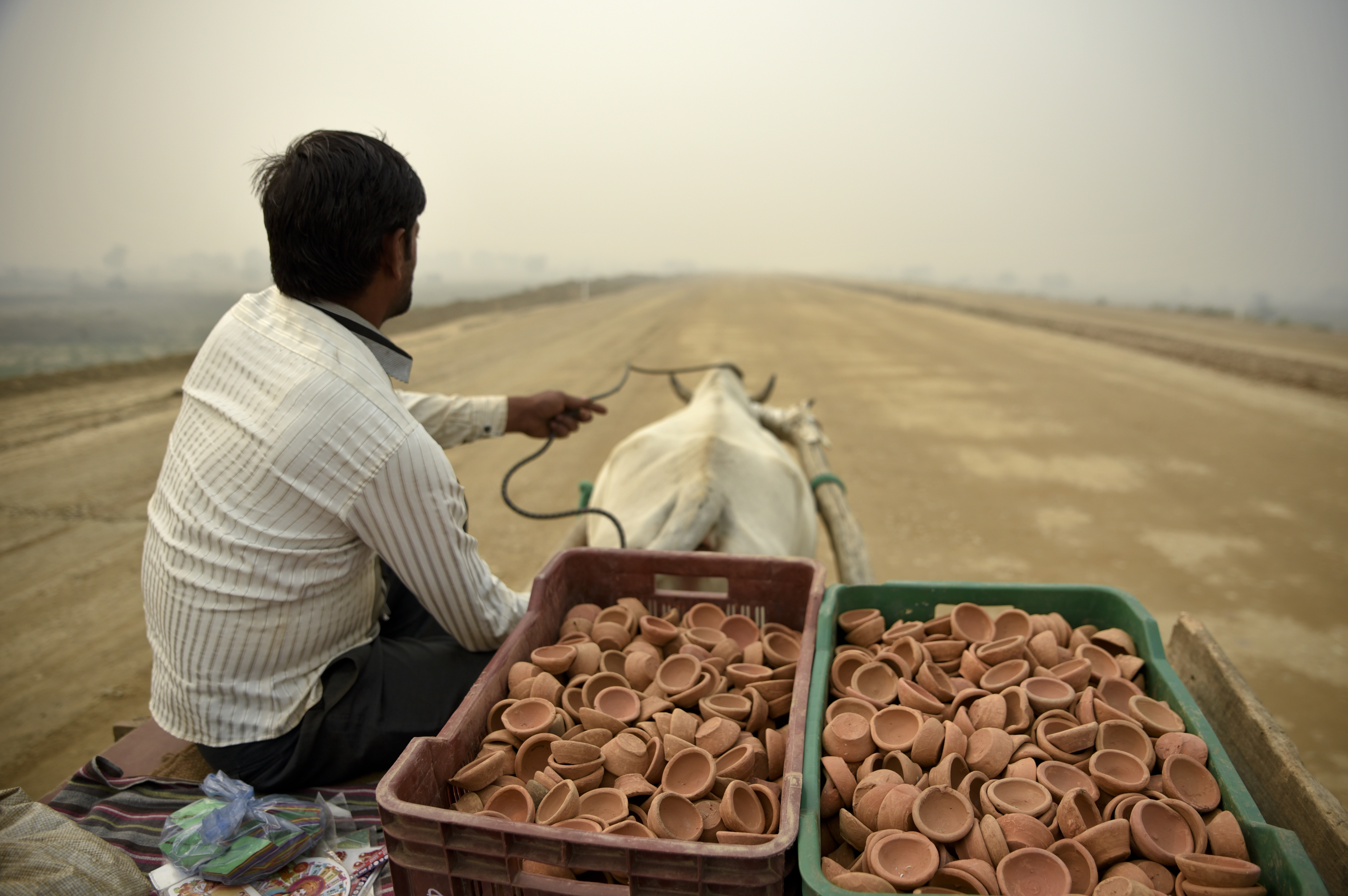 A man selling traditional earthen lamps ahead of Diwali festival, rides a bullock cart through an under construction road on a foggy day in Greater Noida, near New Delhi - AP