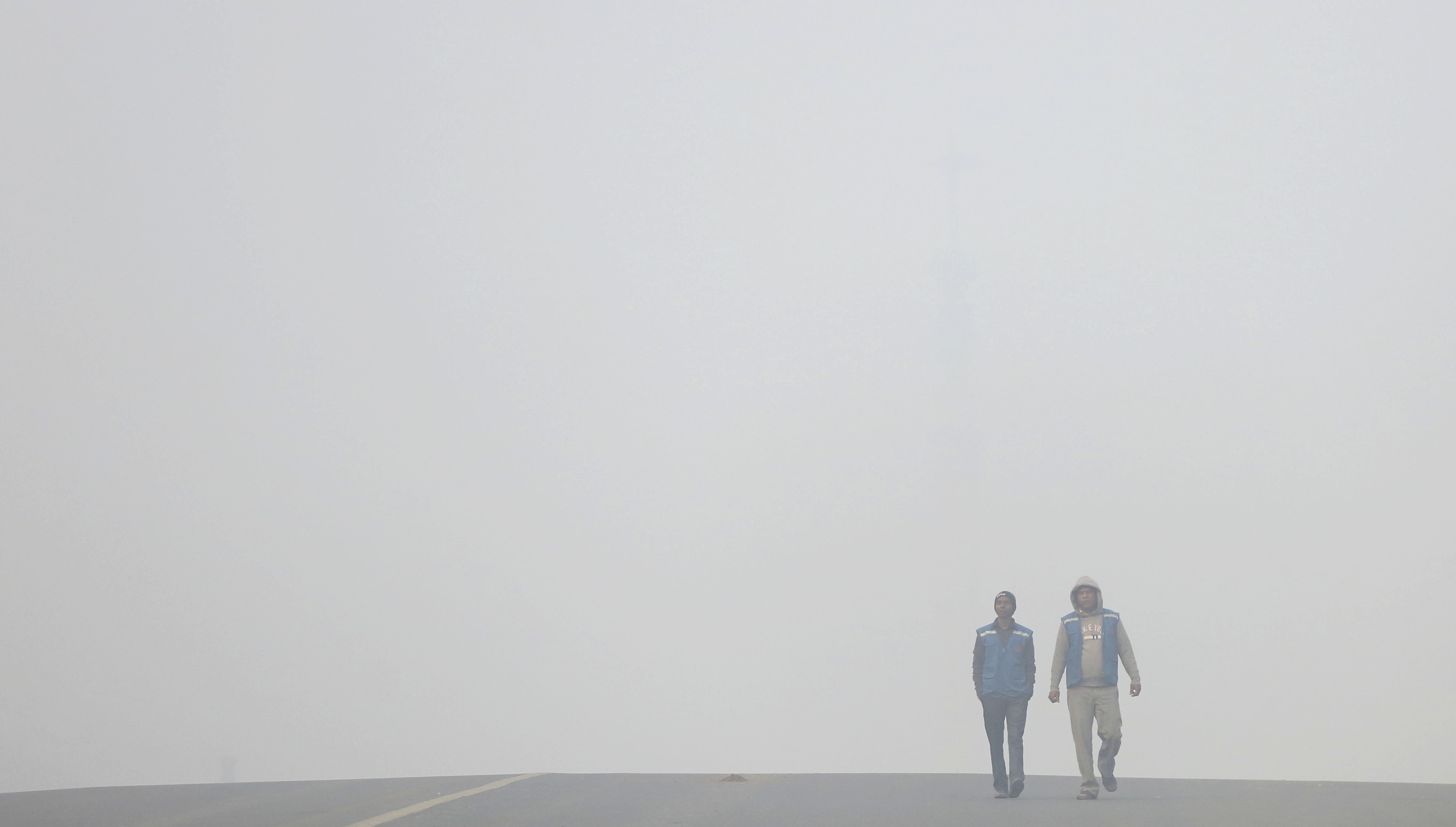 People walk on a road enveloped by thick fog in New Delhi - AP