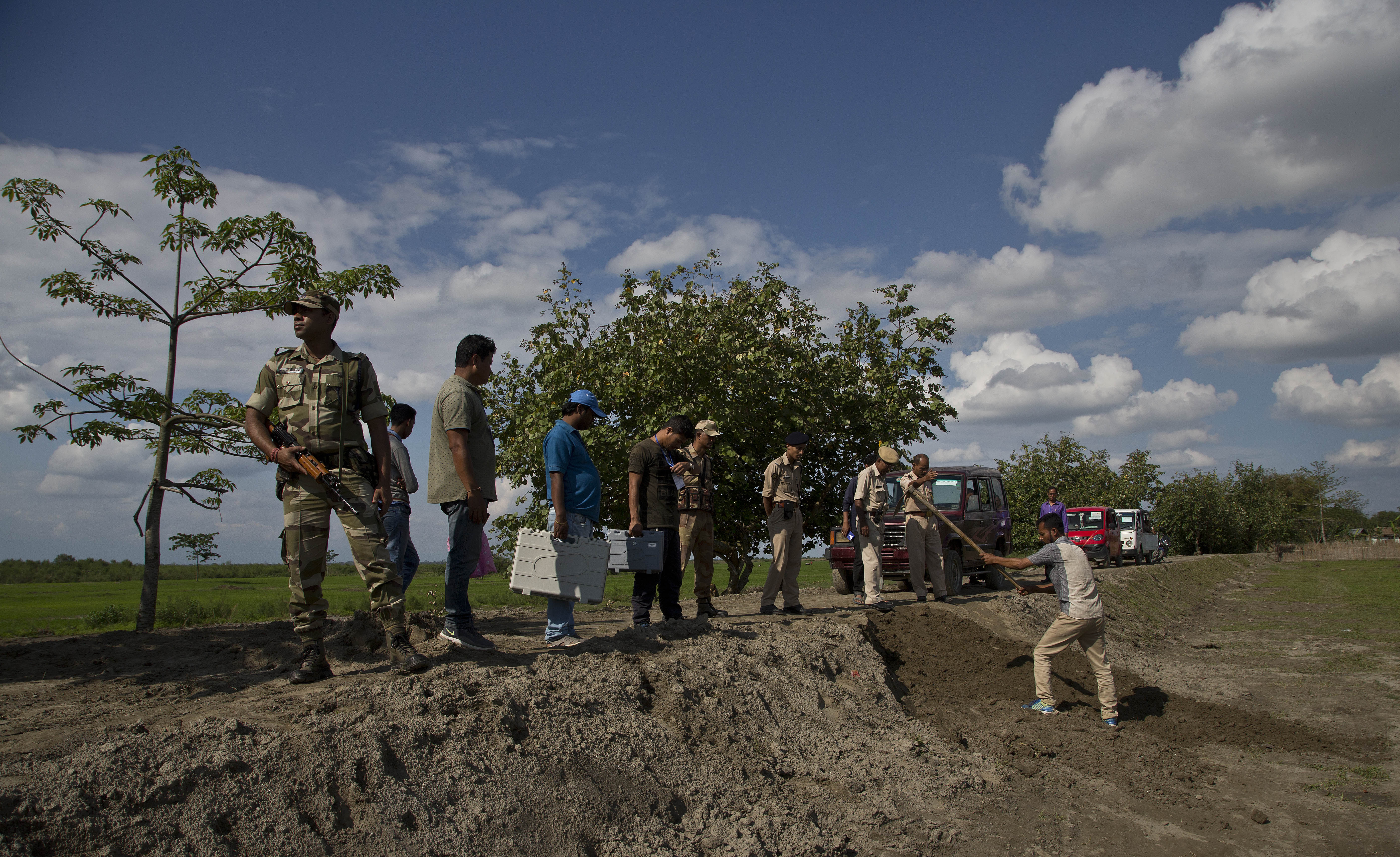 Indian election officials and paramilitary soldiers with election materials stand and watch as a driver fills up soil to make a diversion on a newly constructed earthen road along the river Brahmaputra on the eve of first phase of general election in Majuli, Assam - AP
