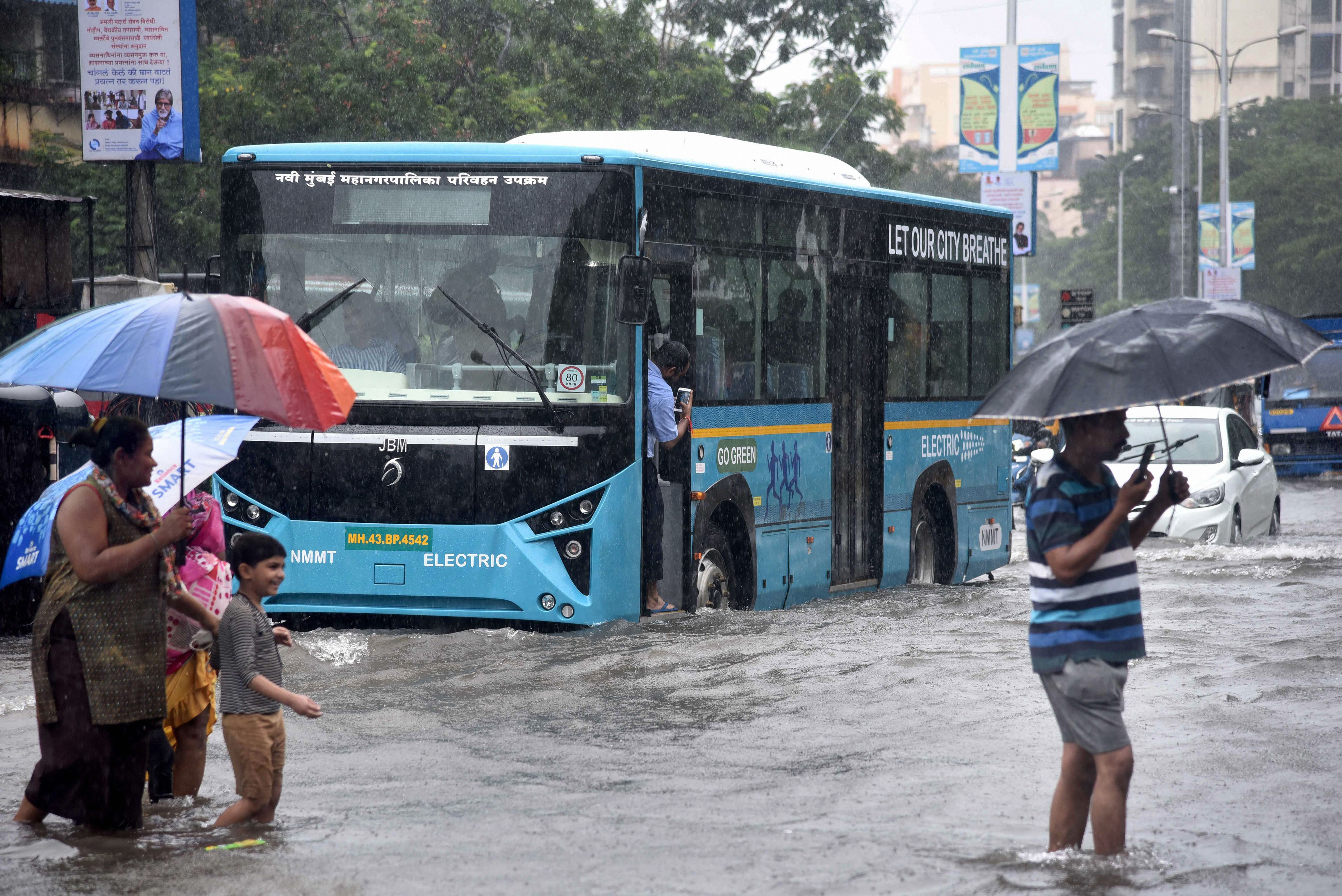 Residents cross a flooded road as vehicles ply on it, following heavy monsoon rains at Vashi in Navi Mumbai - PTI
