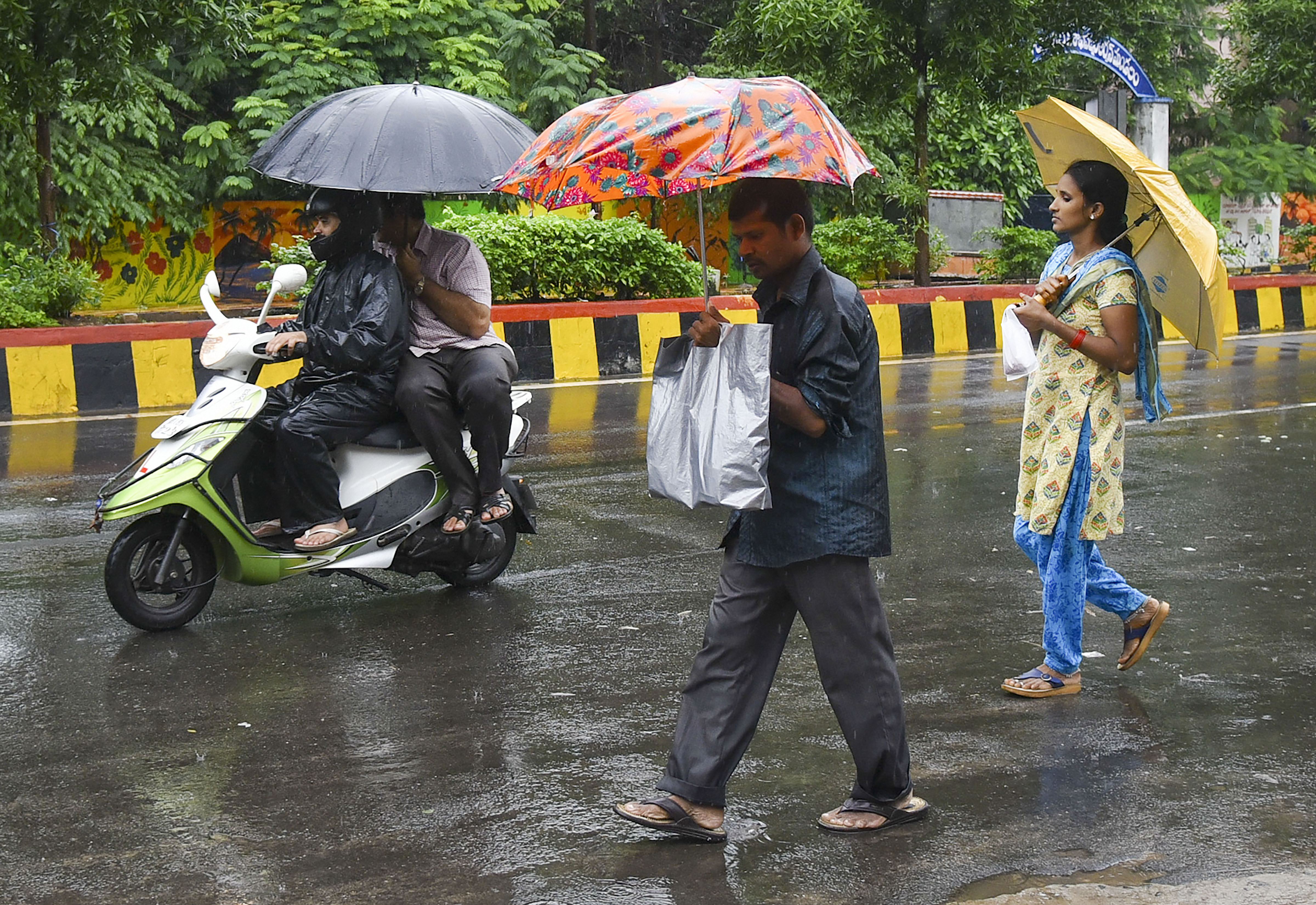 Pedestrians and commuters pave their way during monsoon rainfall, in Visakhapatnam - PTI